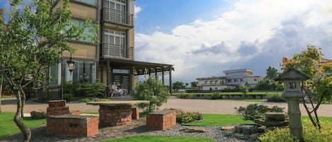 Een modern gebouw met twee verdiepingen, een balkon en een tuin met bakken van baksteen en een kleine fontein.