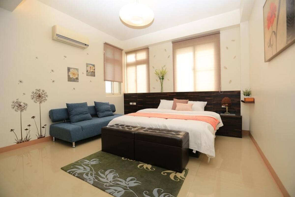 A bedroom with a bed, a sofa, an ottoman, a rug, and wall decorations.