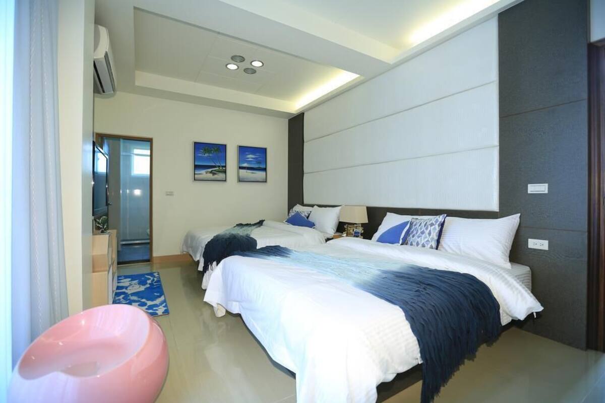 A modern hotel room with two beds, a large window, and a bathroom with a shower and toilet.