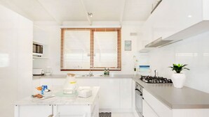 Une cuisine moderne avec des meubles blancs, une cuisinière à gaz, un four à micro-ondes et une fenêtre équipée de stores.
