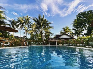 A swimming pool with clear blue water, surrounded by palm trees and a thatched-roof structure. - The Village Siargao (General Luna)