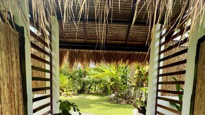 A covered outdoor area with a thatched roof, a gravel pathway, and a grassy lawn. - The Village Siargao (General Luna)