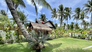 A tropical garden with a thatched-roof hut, palm trees, and well-maintained grass. - The Village Siargao (General Luna)