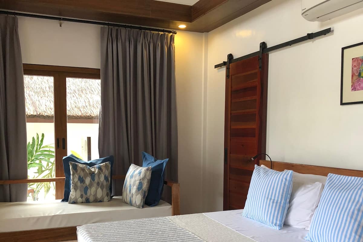 A bedroom with a wooden bed, a window seat with curtains, and a view of the outdoors.