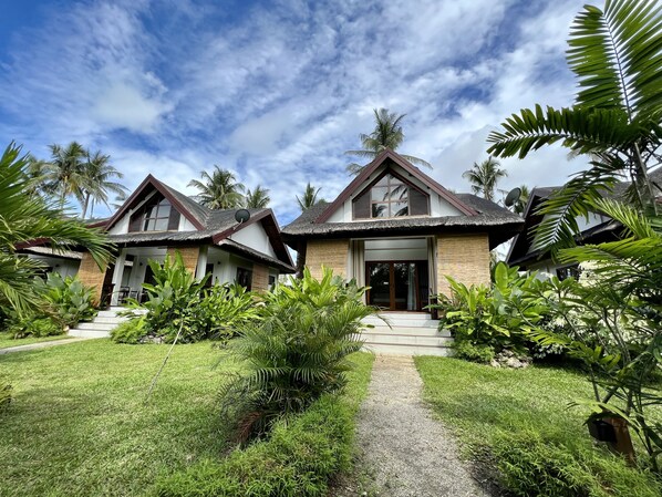 A bungalow-style resort with a thatched roof, surrounded by lush greenery and palm trees. - The Village Siargao (General Luna)