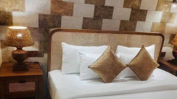 A neatly made bed with two pillows, a wooden headboard, a nightstand with a lamp, and a patterned wall. - Sea Cloud Dalawella (Unawatuna)