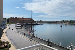 A waterfront promenade with a dock, boats, and buildings in the background.