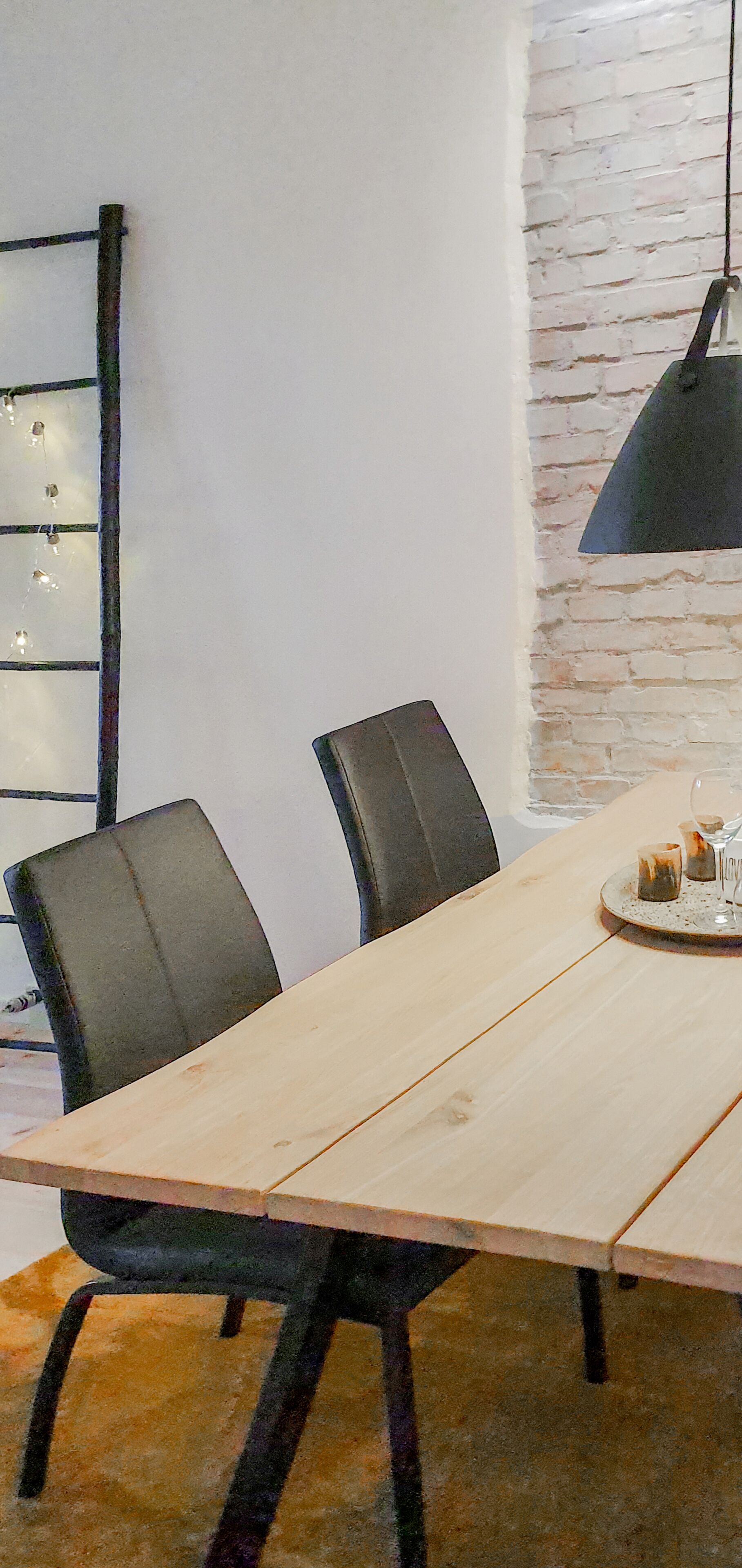 Un comedor con una larga mesa de madera, sillas negras y un colgante.