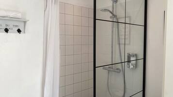 A glass-enclosed shower with a white tiled wall, a white shower curtain, and a shelf with a towel.