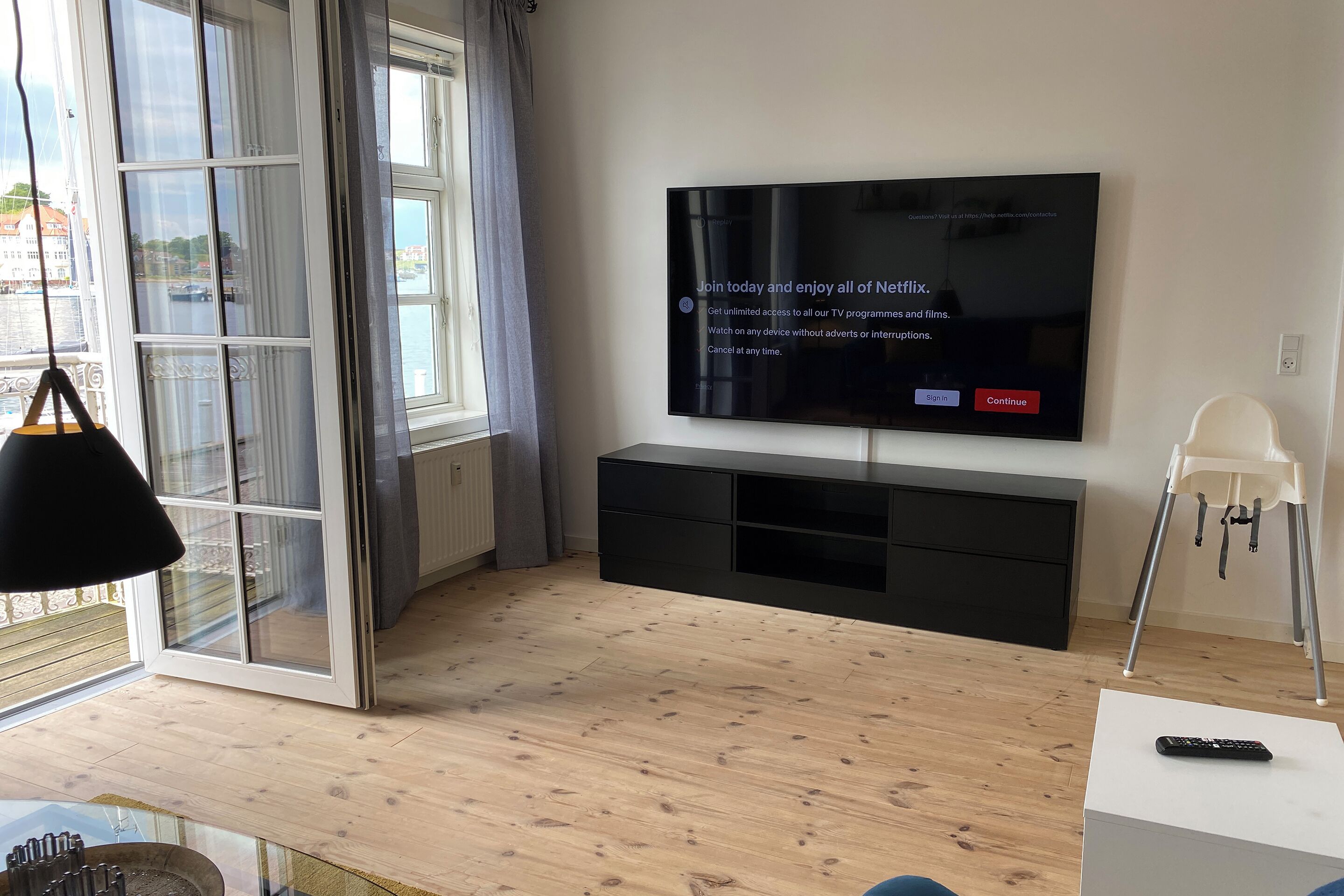 A modern living room with a large flat-screen TV mounted on a black entertainment unit, a glass coffee table, and a white chair.