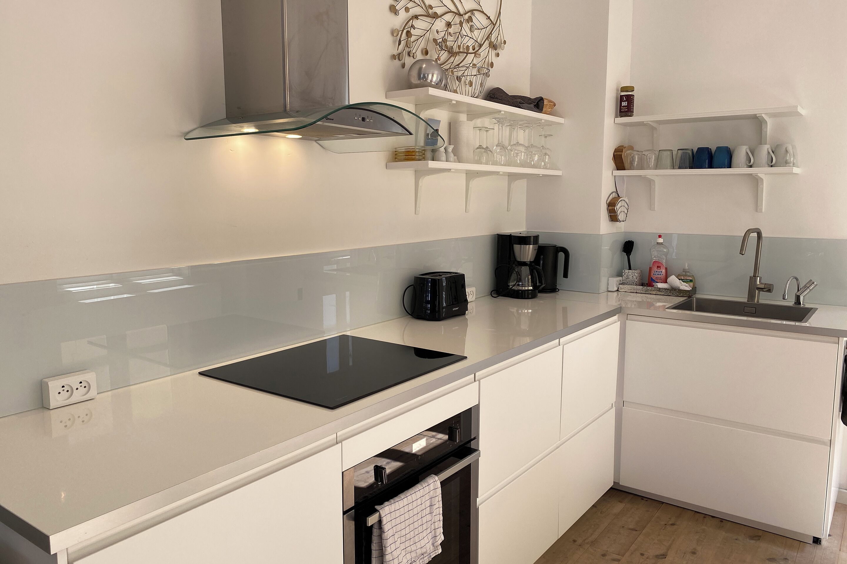 Una cocina moderna con armarios blancos, encimera negra, horno empotrado y campana extractora de acero inoxidable.