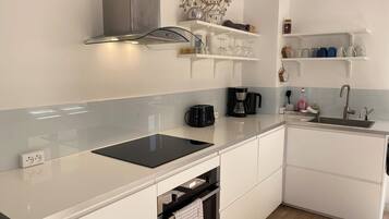 Una cocina moderna con armarios blancos, encimera negra, horno empotrado y campana extractora de acero inoxidable.