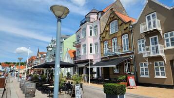 A cobblestone street lined with colorful buildings, outdoor seating, and a signboard.