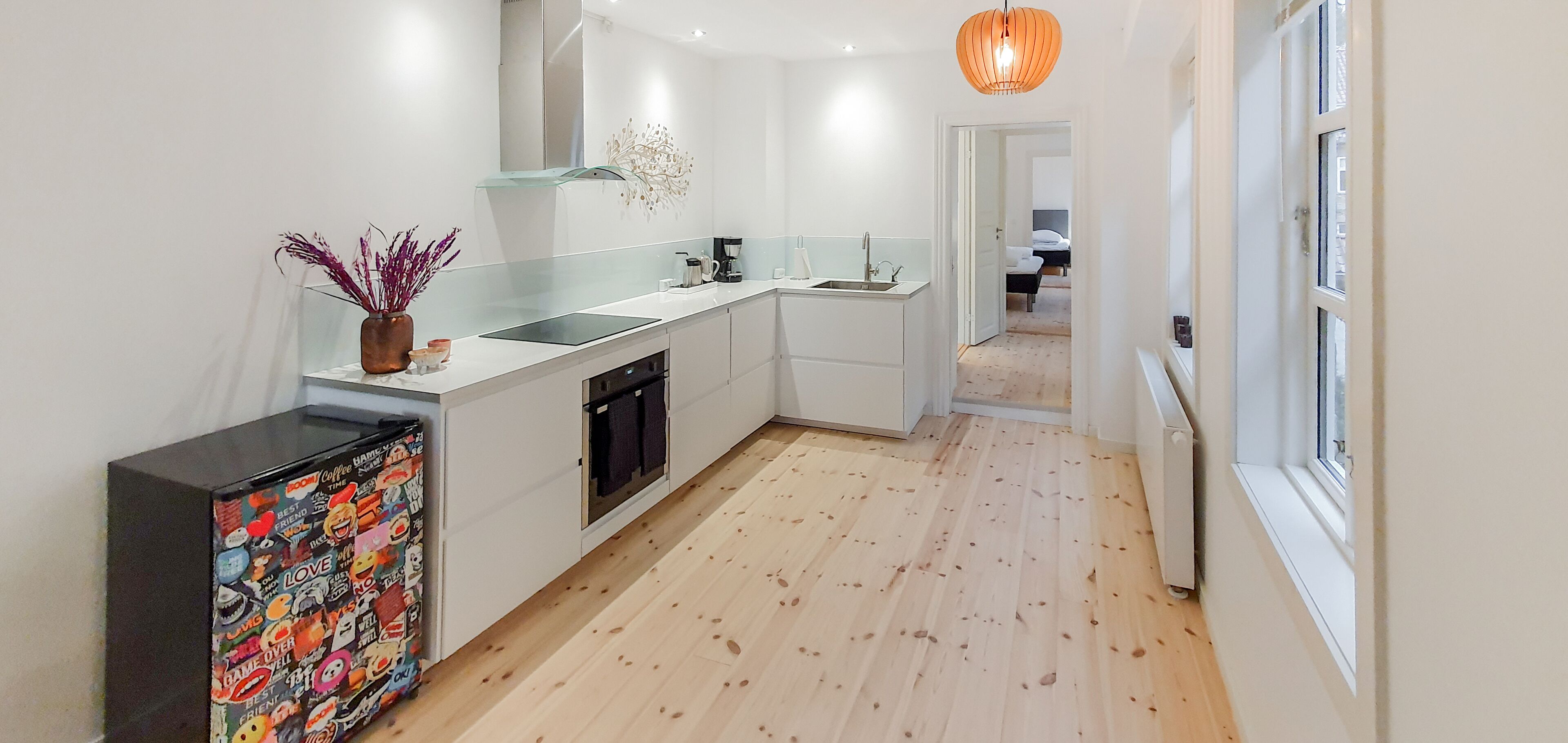 A modern kitchen with white cabinets, a glass backsplash, and a wooden floor.