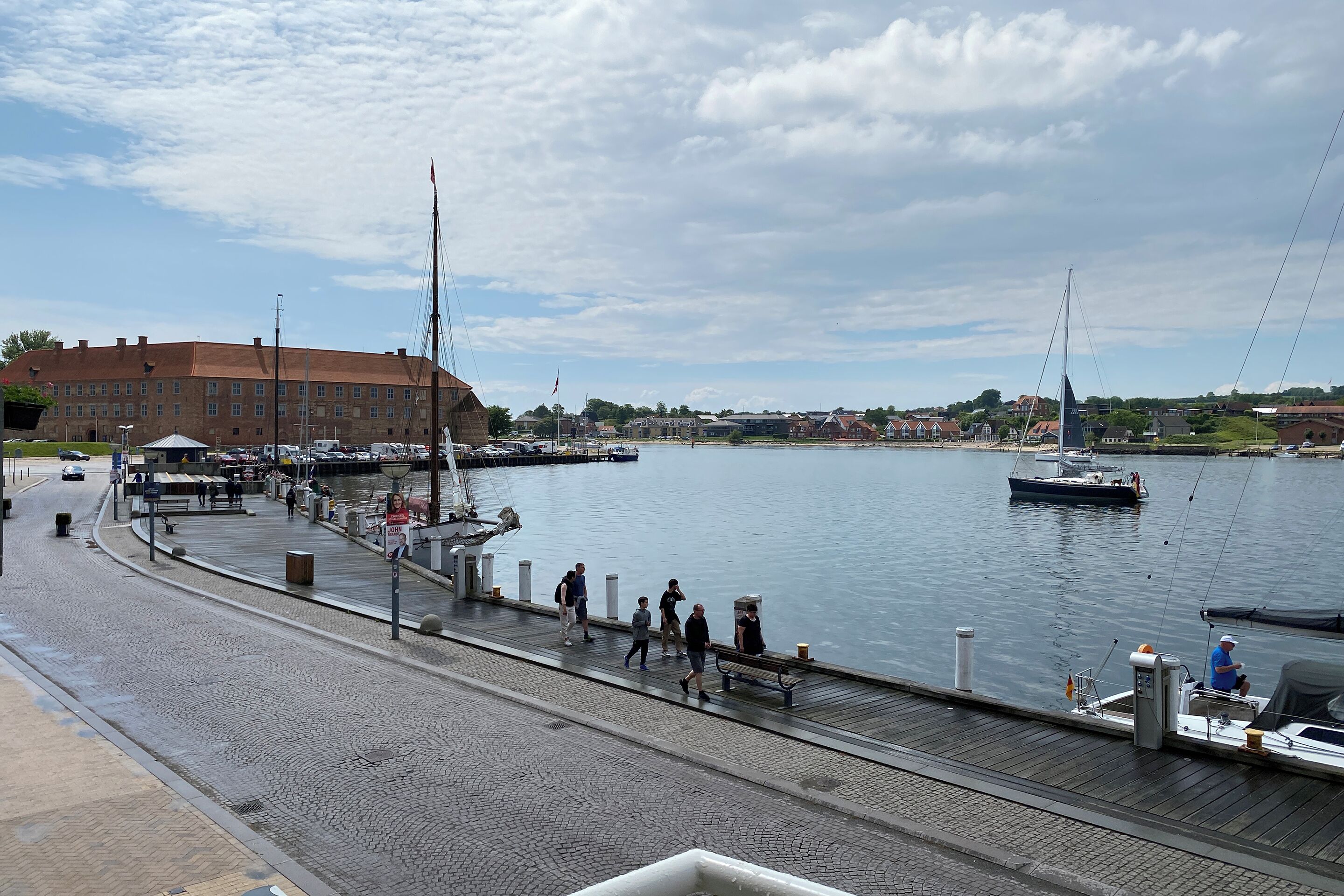 Un paseo marítimo con muelle, barcos y un edificio al fondo.