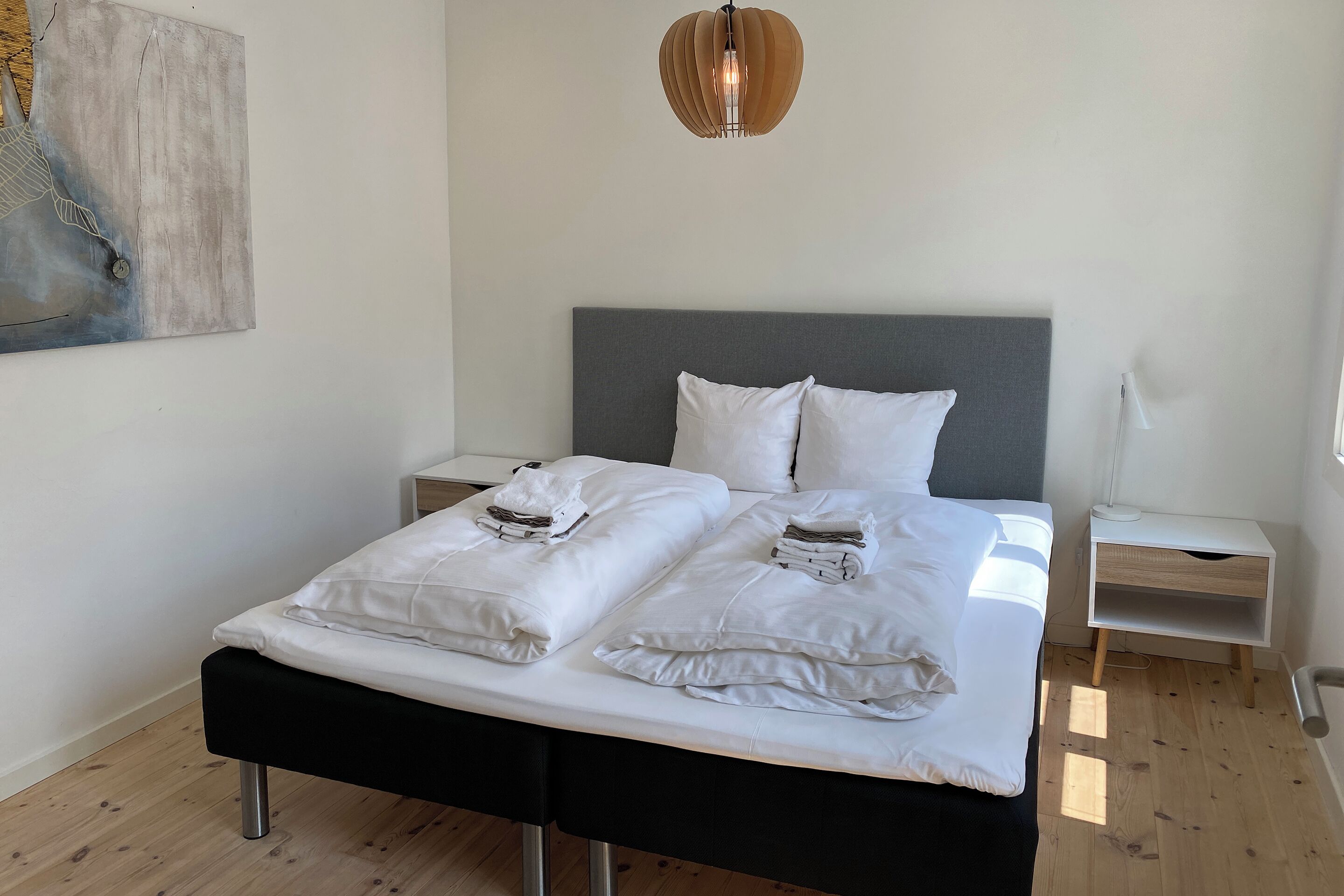 A neatly made bed with white linens and pillows, a grey headboard, and a wooden floor.