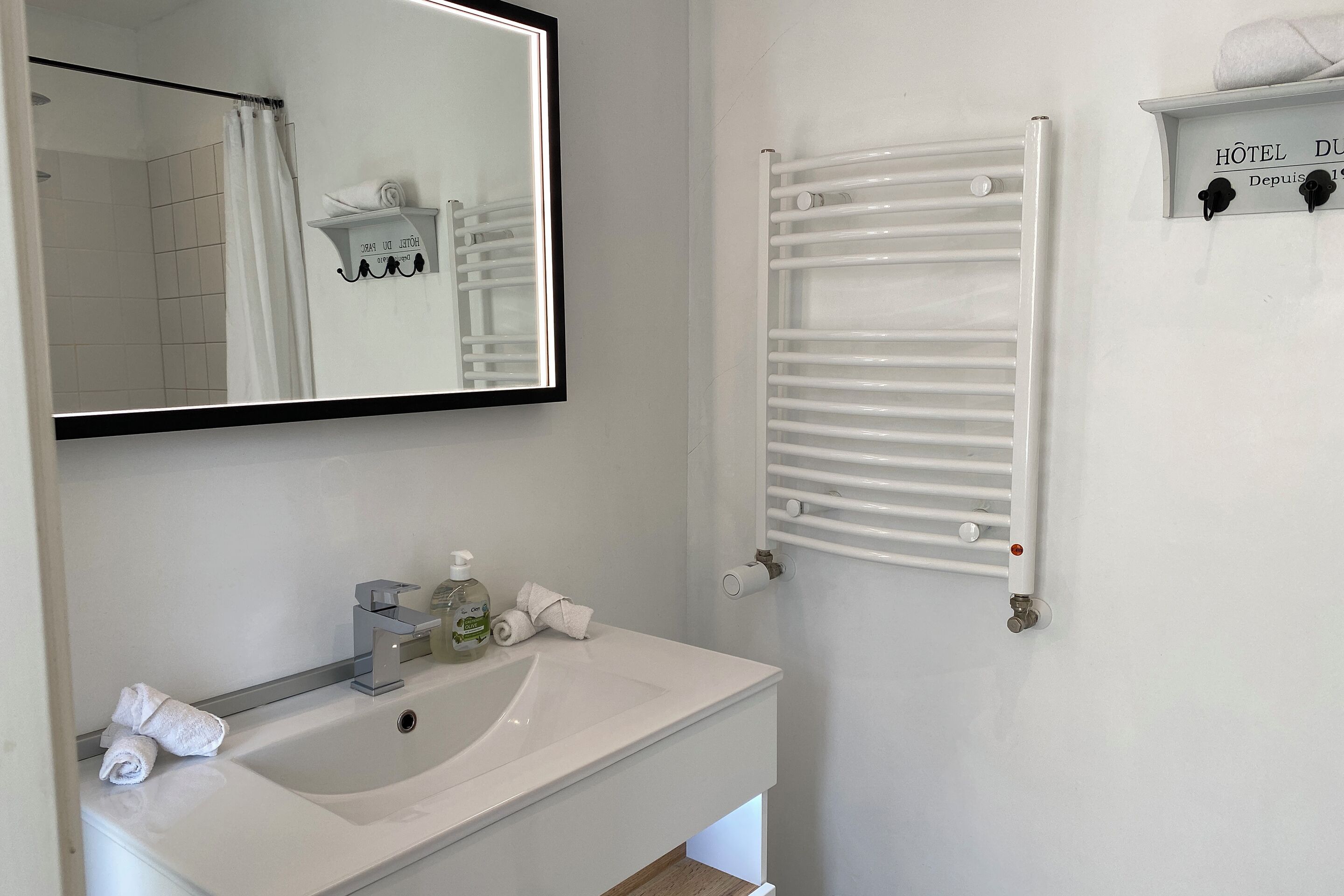 A bathroom with a white sink, a mirror, a towel rack, and a towel warmer.