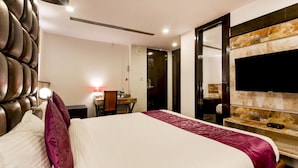 A hotel room with a large bed, a desk with a chair, a TV mounted on the wall, and a door leading to a bathroom. - Treebo Tryst F One (Hyderabad)