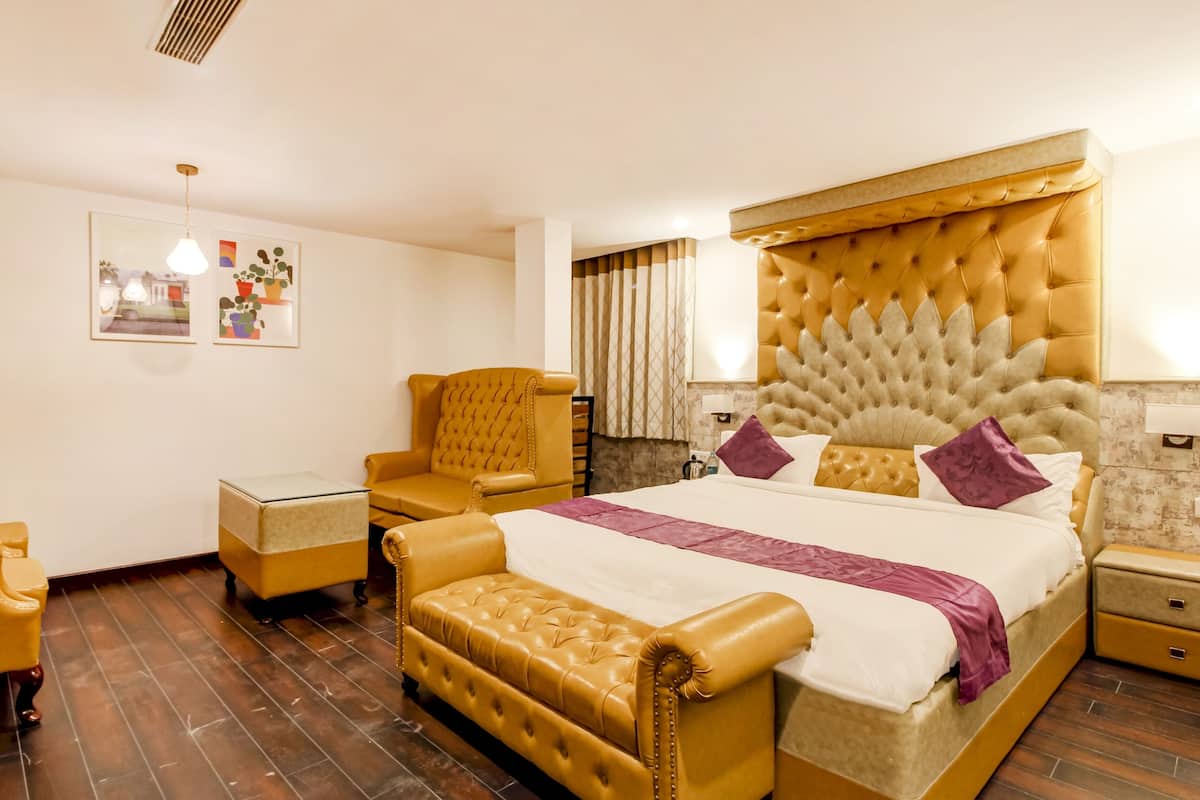 Quarto de hotel com uma cama grande, área de estar com uma poltrona e apoio para os pés, uma mesinha e uma TV fixada na parede.