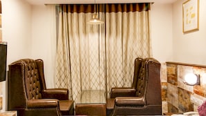A room with two leather armchairs, a glass-top table, a patterned curtain, a pendant light, a framed picture, and a wall-mounted light fixture. - Treebo Tryst F One (Hyderabad)
