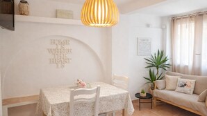 Un comedor con mesa, sillas, lámpara colgante, sofá y pared con una frase decorativa.