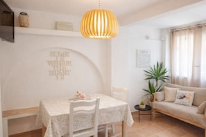 A dining area with a table, chairs, a hanging light fixture, a sofa, and a wall with a decorative phrase.