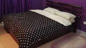 Makuuhuone, jonka seinät ovat violetit, sängyssä on pilkkukuviollinen päiväpeite ja sängynpääty on puuta.