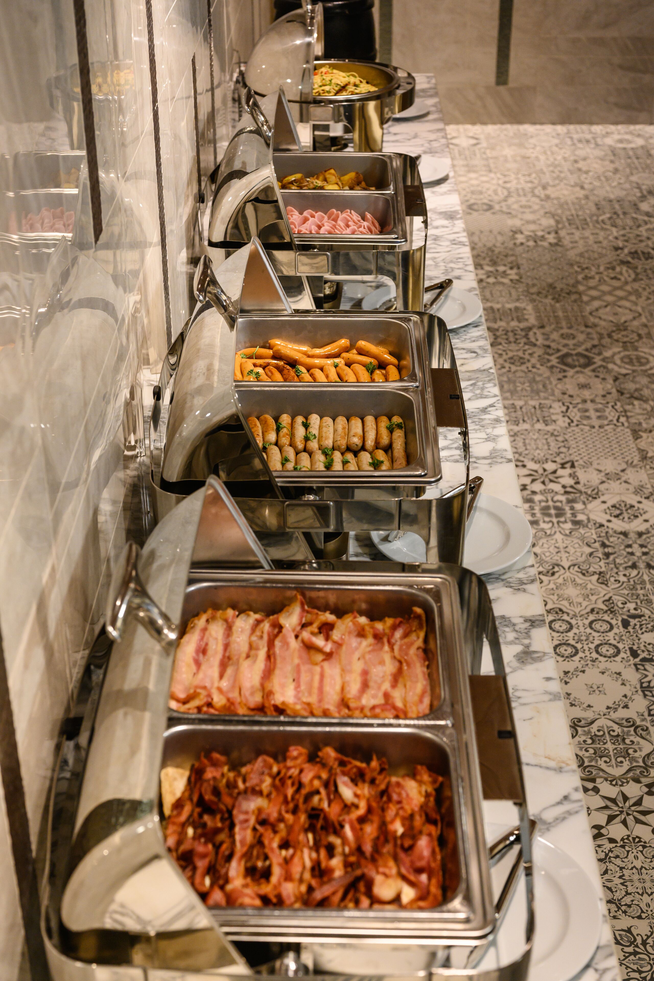 A buffet line with various food options including bacon, sausages, and other meats.