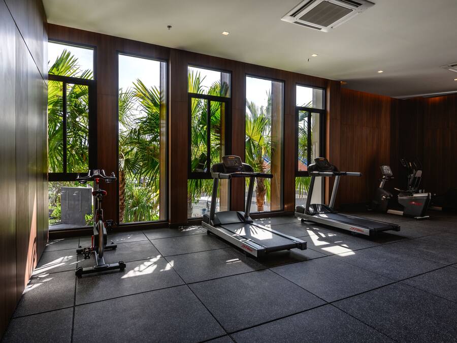 A gym with treadmills, a stationary bike, and a rowing machine, large windows with a view of palm trees.