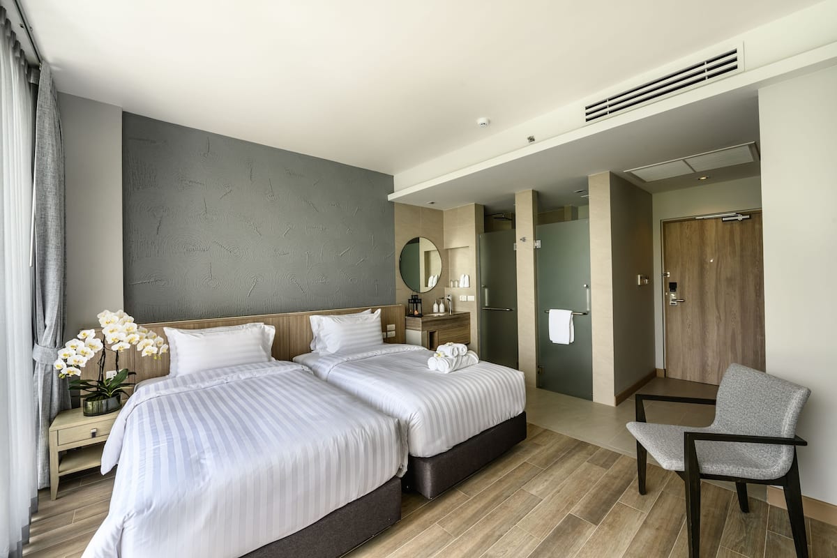 Una habitación de hotel moderna con dos camas, un espacio para sentarse, un baño y vistas al pasillo.