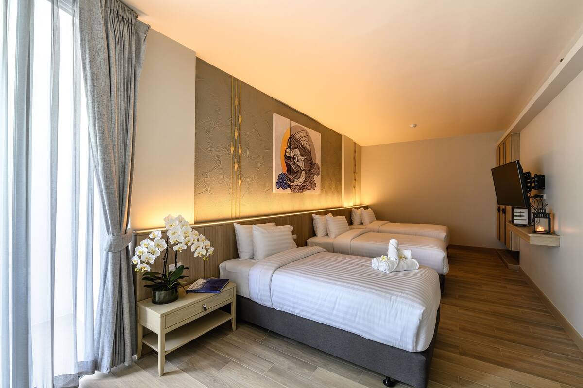 Una habitación de hotel moderna con dos camas, una mesita de noche con lámpara, una obra de arte en la pared y un pequeño estante con objetos.