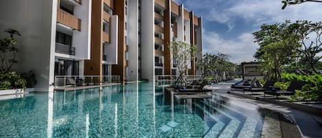 A modern hotel with a clear pool, wooden balconies, and a well-maintained garden area.