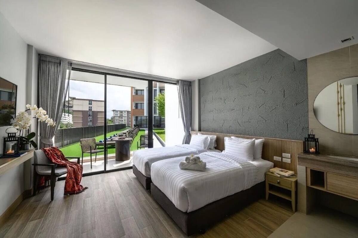 Habitación de hotel moderna con una cama grande, un área de descanso con una silla y una mesa, un balcón con vistas a la ciudad y un espejo grande en la pared.