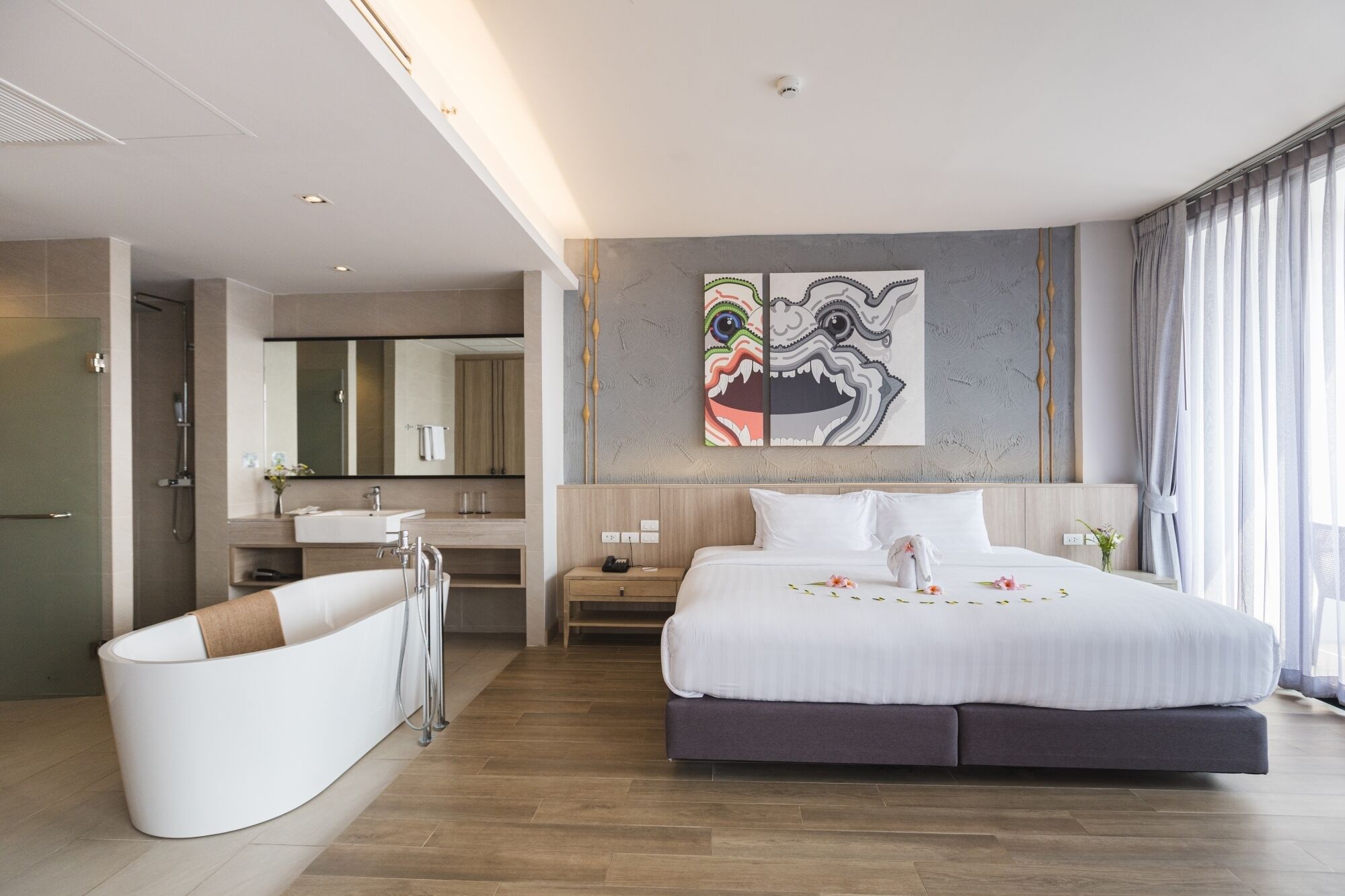 Una habitación de hotel moderna con una cama grande, un baño separado con bañera, un espejo amplio y obras de arte en la pared.