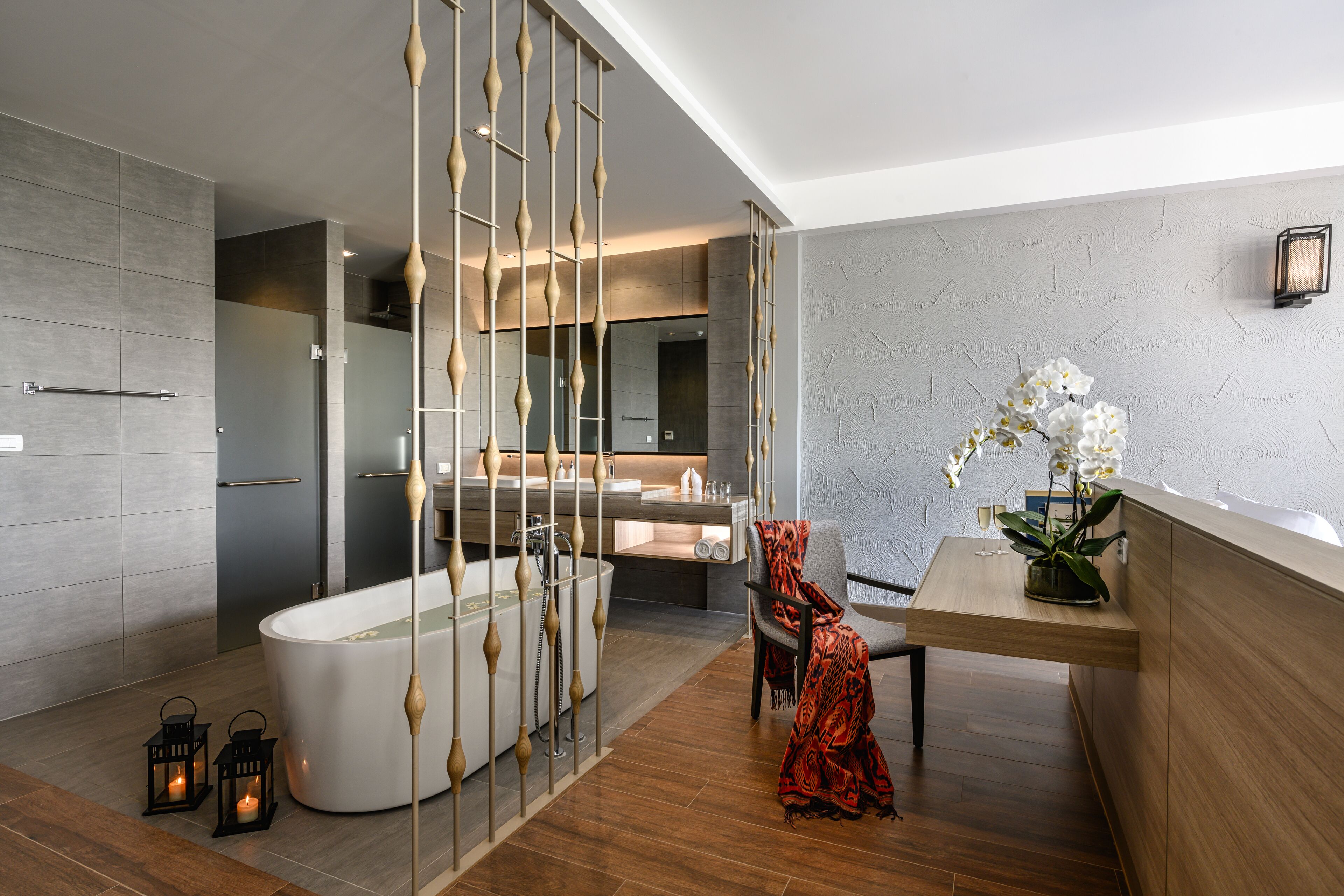 A modern bathroom with a freestanding bathtub, a wooden partition, and a small table with a potted orchid.
