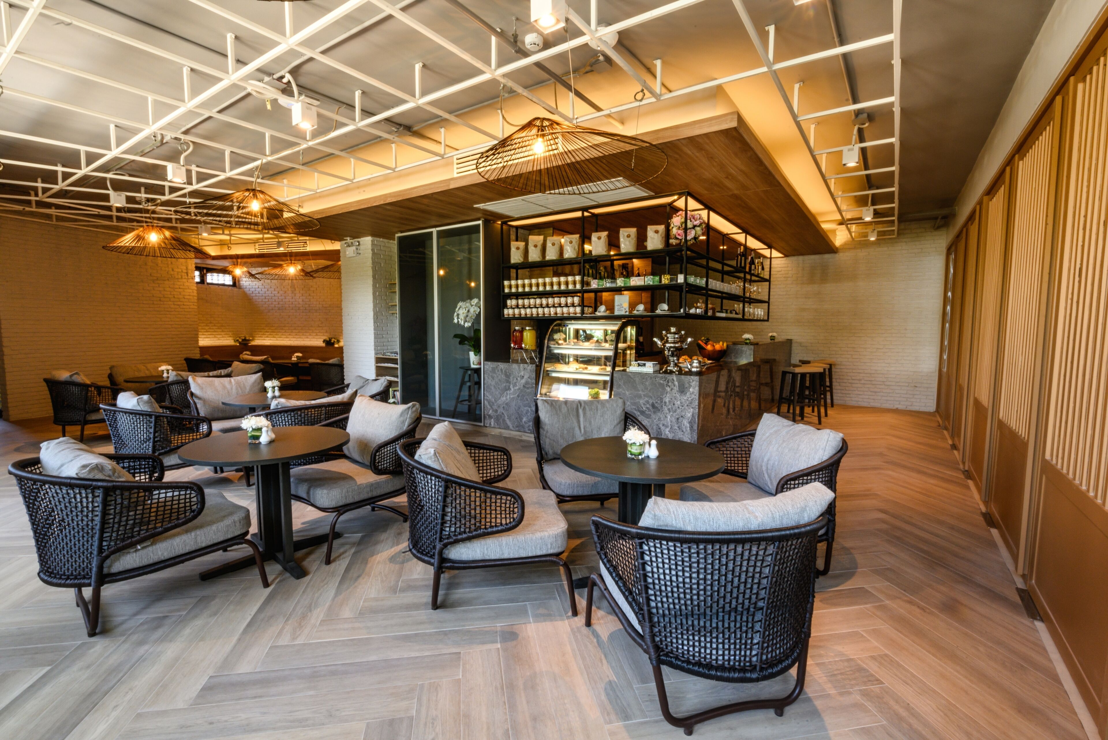 Uma área de estar interna moderna, com cadeiras de vime e mesas redondas, um bar com prateleiras cheias de garrafas e uma parede de tijolos.