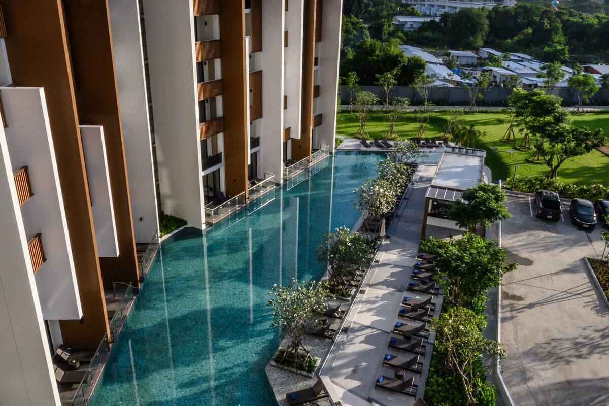Un hotel moderno con piscina en la azotea, varios balcones y vistas del paisaje circundante.