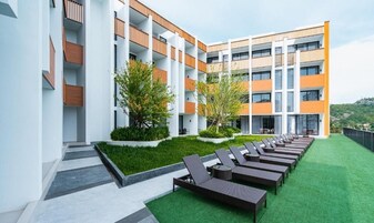 A modern building with multiple balconies, a rooftop garden with artificial grass and sun loungers, and a view of a hilly landscape.