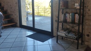 Une pièce avec un sol carrelé, une porte-fenêtre coulissante donnant sur l’extérieur, une bibliothèque et un petit escalier.
