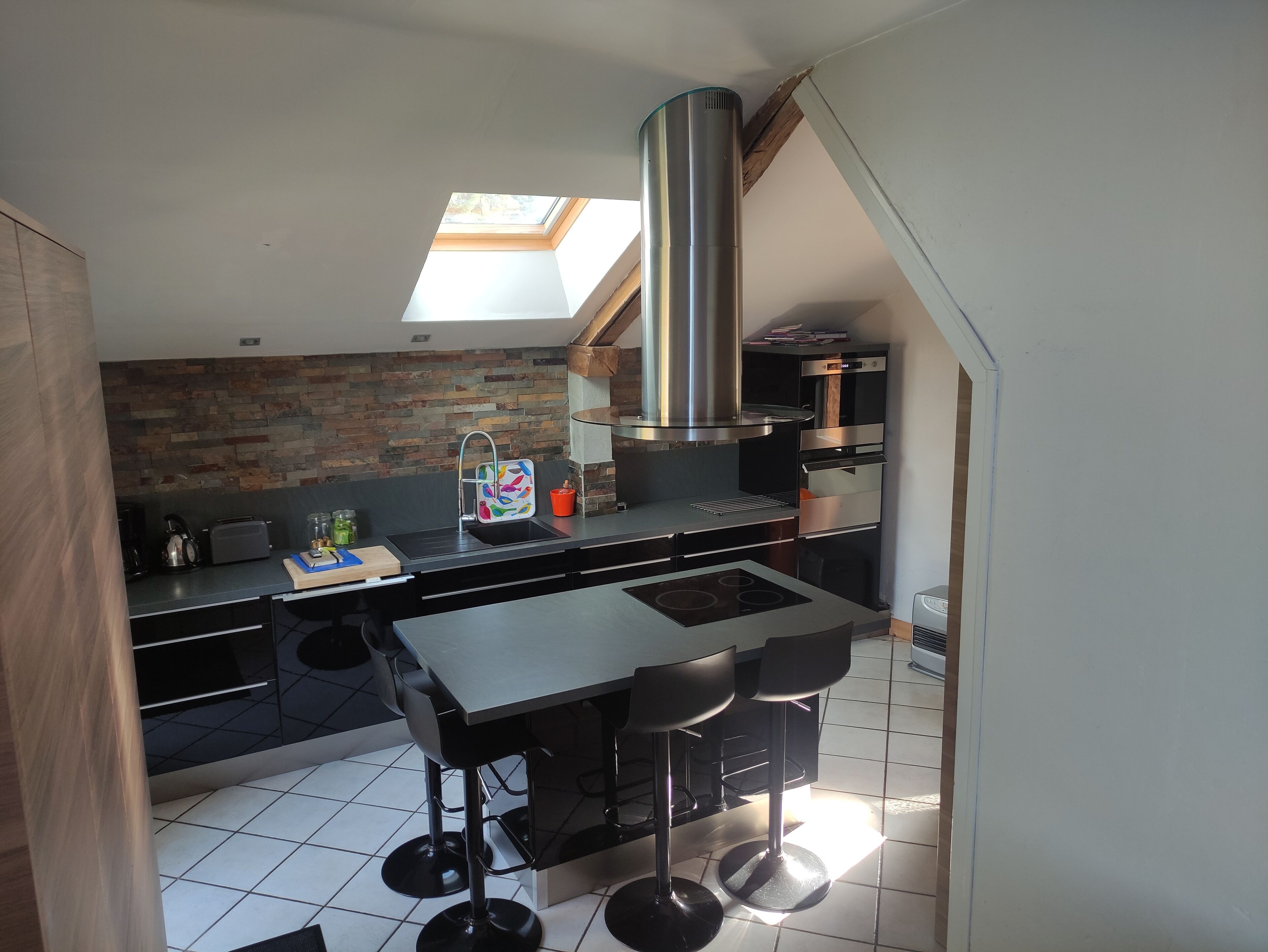 A modern kitchen with a skylight, a stainless steel range hood, and a built-in oven.