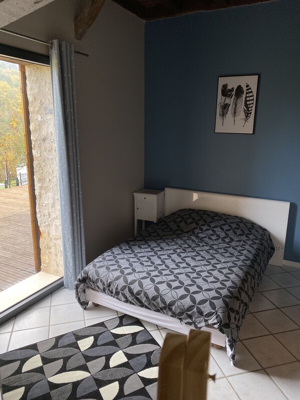 A bedroom with a bed, a nightstand, a window with curtains, and a wall-mounted picture.