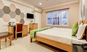 A hotel room with a bed, desk, chair, and a TV on the wall.