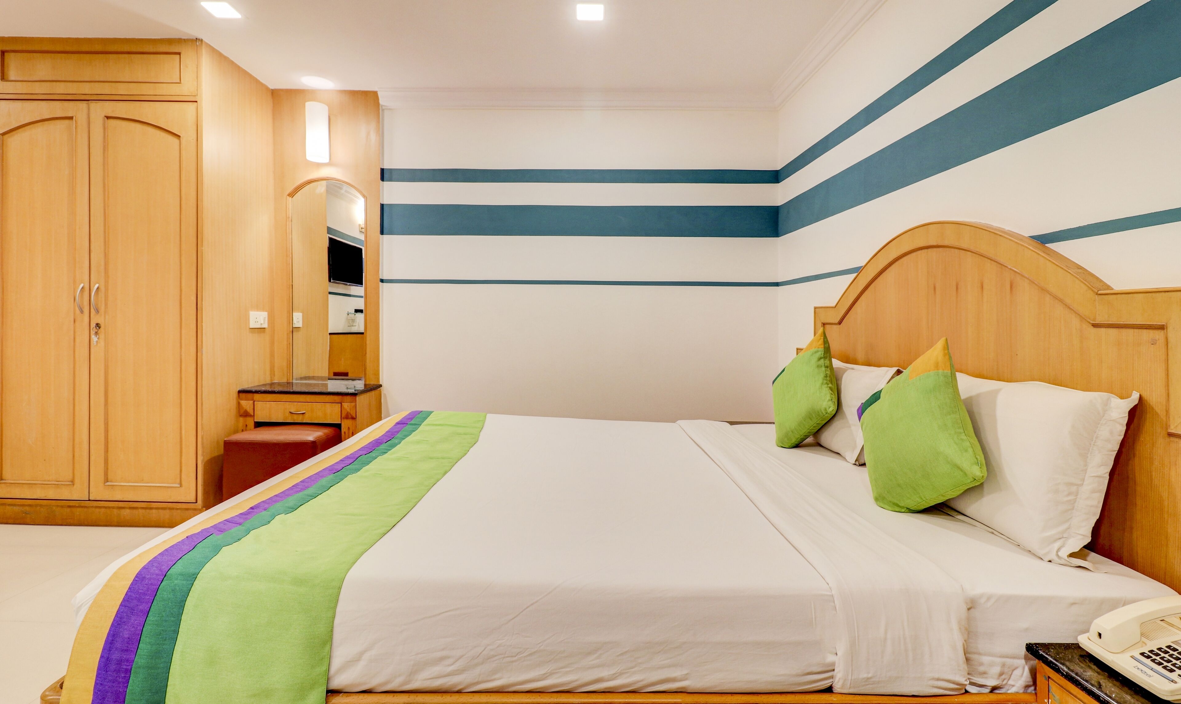 A hotel room with a bed, a wooden wardrobe, a bedside table, and a mirror.