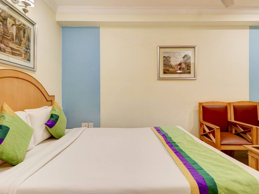 Quarto de hotel com cama, duas almofadas, uma cadeira e duas imagens emolduradas na parede.