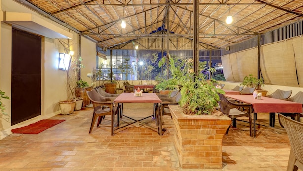 An indoor patio area with brick flooring, wooden tables, wicker chairs, and potted plants. - Treebo Terminus, Koramangala 5th Block (Bengaluru)