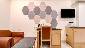A compact hotel room with a modern design, featuring a hexagonal wall decoration, a flat-screen TV, a wooden desk with a chair, a small kitchenette, and a sofa. - Treebo Terminus, Koramangala 5th Block (Bengaluru)