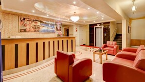 A hotel lobby with a reception desk, red leather sofas, a chandelier, a mural, and a staircase. - Treebo Terminus, Koramangala 5th Block (Bengaluru)