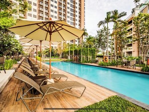 Relax by the pool surrounded by lush tropical plants and trees, with comfortable sun loungers and umbrellas for shade.