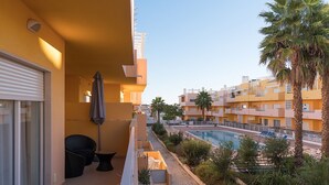 Varanda com vista para uma piscina, cercada por palmeiras e vegetação.