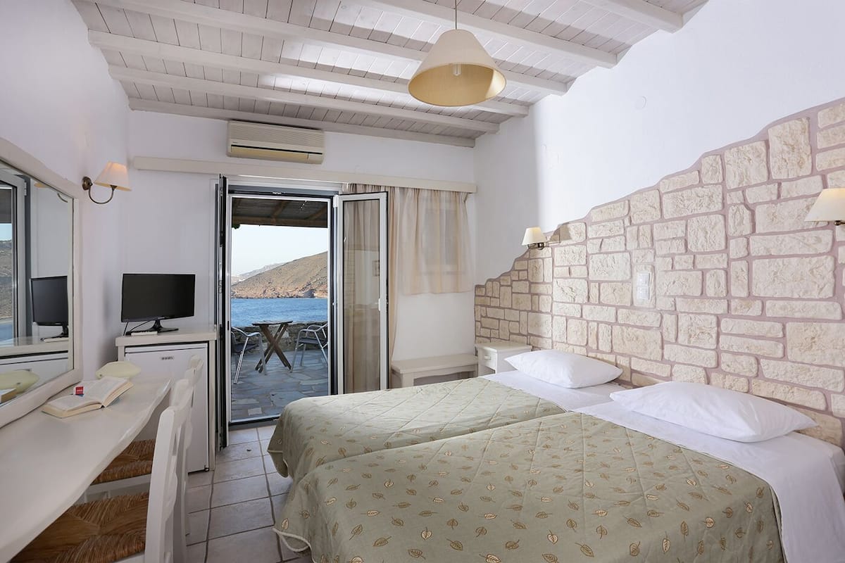 A bedroom with a stone headboard, a desk with a computer, and a view of the sea through an open door.